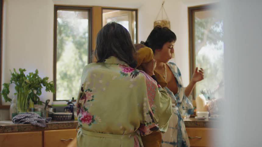 A grandmother twirls her little grandson around while his mother stands at the counter and eats