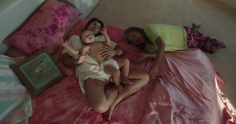 Two women playing with a toddler over the bed inside a bedroom at home
