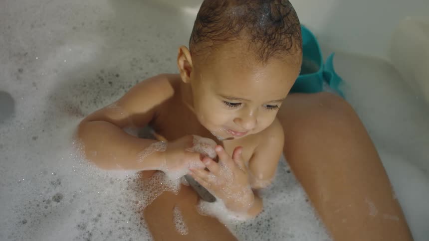 A baby sits in a bathtub of bubbles with his mom