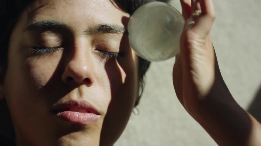 A woman massages her face with a ball in the sunshine