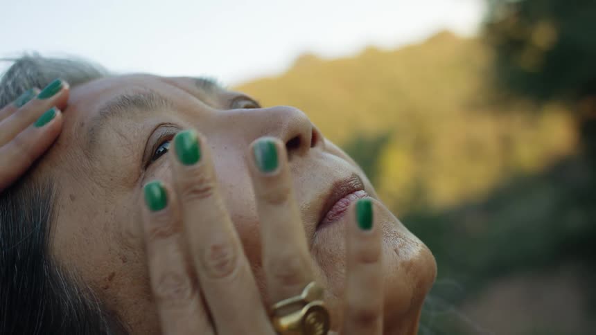 An elderly woman leans her head back outdoors as another woman rubs and pats her face