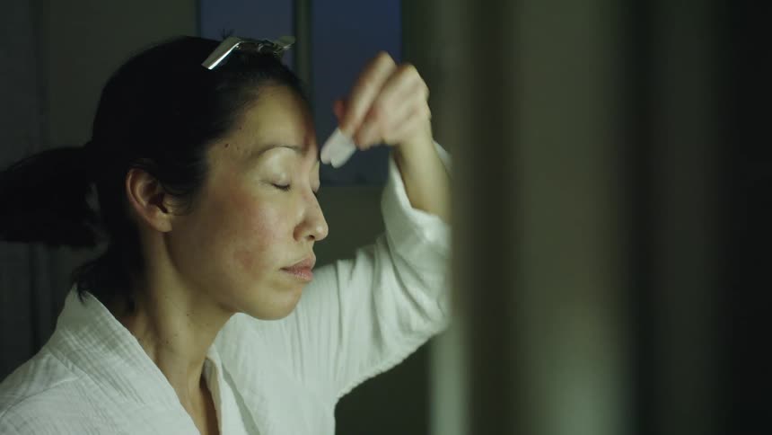 Young woman wearing a white robe scrapes the skin on her forehead with a plastic tool