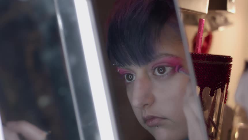 Young woman applying colorful makeup in front of a mirror at home