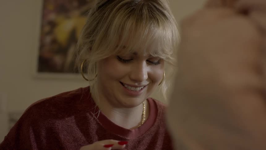 A woman is sitting indoors and applying makeup