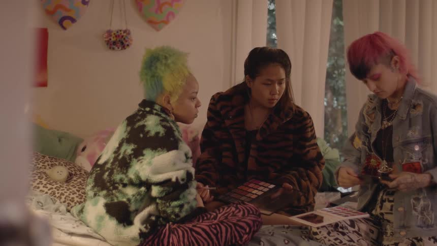 Fashionable diverse young women consult over makeup while sitting in bedroom