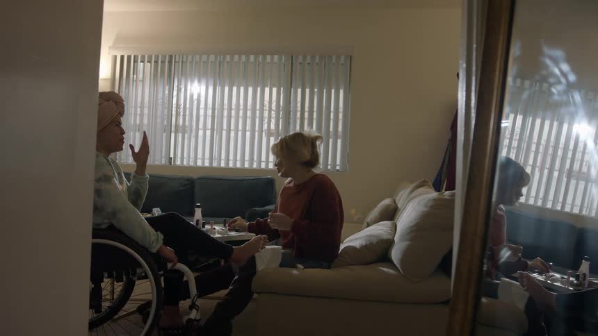 A woman in a wheelchair sits with her foot in another womans lap as she waits to have her toes painted