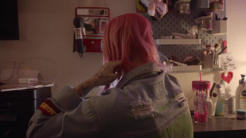 A woman uses a hair iron to straighten her hair while looking into a small illuminated mirror