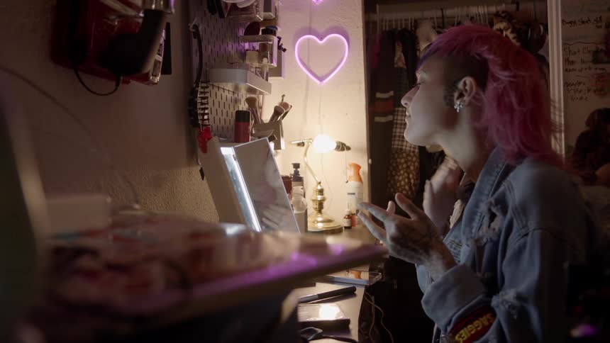 A teenage girl sits in front of a mirror and puts on make up