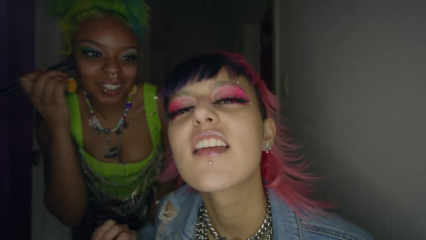 Two women are doing their makeup in a mirro