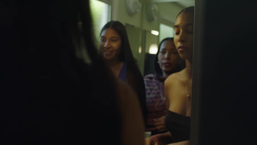 Women fashionably dressed put on makeup and jewelry standing in group in front of mirror
