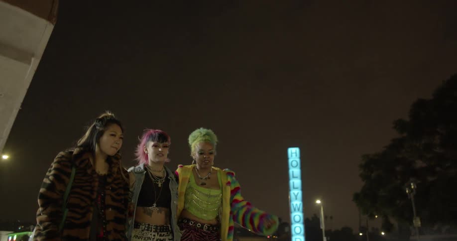 Fashionably dressed friends with bright hair dye walk down sidewalk crossing into the intersection