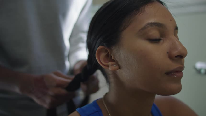 A girl is getting her hair braided by a friend indoors
