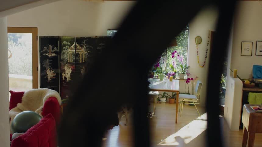 Two women sit at a table in a home by a dog and then the younger woman gets up and walks to her young son and picks him up and takes him to the table