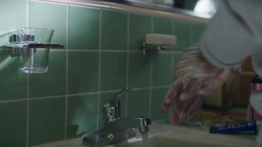 Woman with gray sweater washes her hands with soap in the bathroom