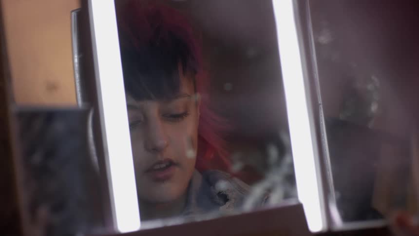 Young woman wearing a piercing on her eyebrow applying makeup in front of a mirror
