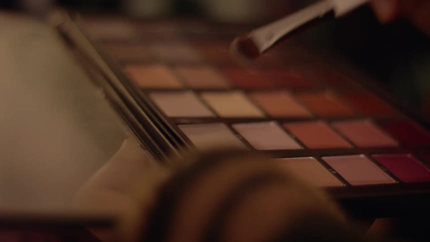 A female pats a brush on a palette with eye shadows