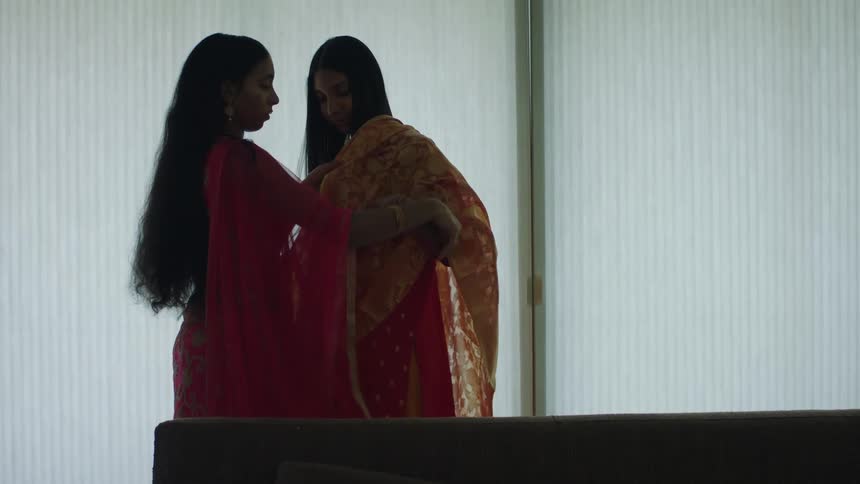A woman helps another woman put a sari over her clothing