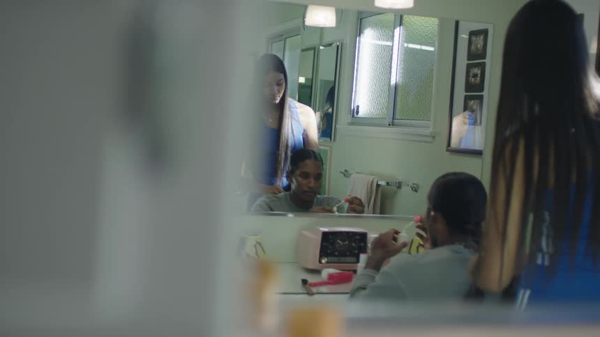 Hair stylist braiding the long hair of a male customer inside a salon in front of a mirror
