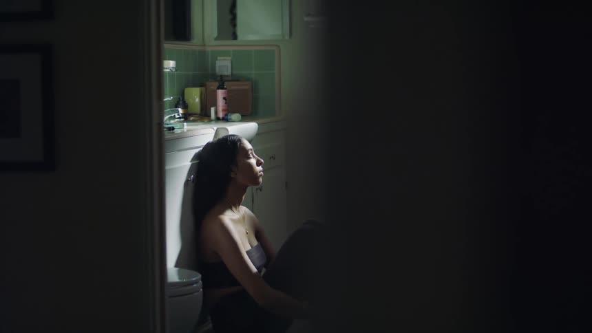 Woman sits on floor in bathroom leaning against cabinet