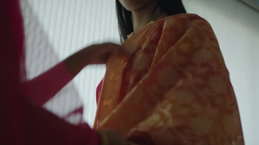 Two women are standing in a room and wearing saris