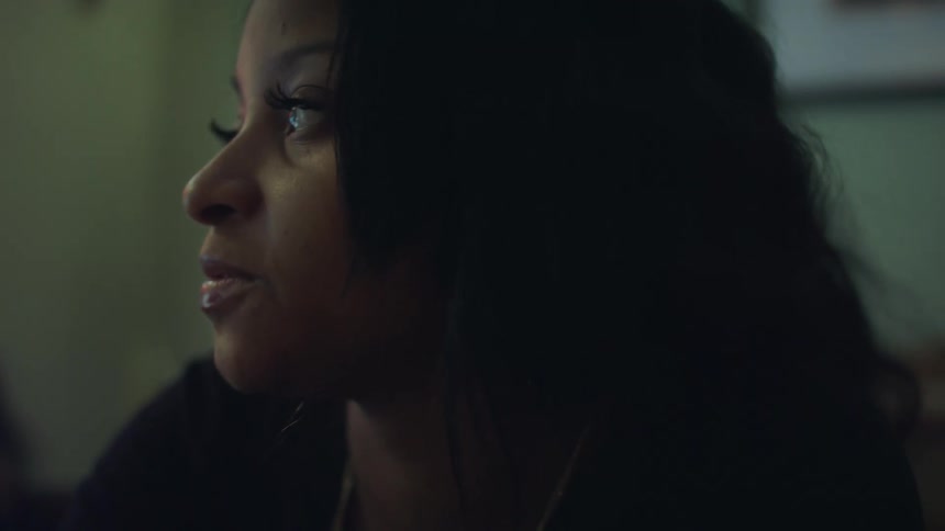 A black woman with long hair is inside a room looking around as she smiles and speaks to someone