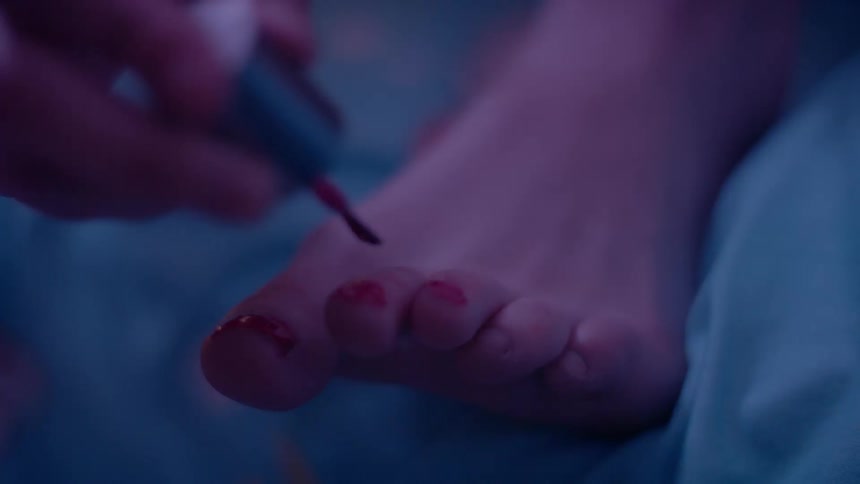 A person is sitting on a bed and painting their toe nails