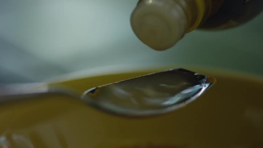 Filling a metal spoon with liquid dripping from a small bottle