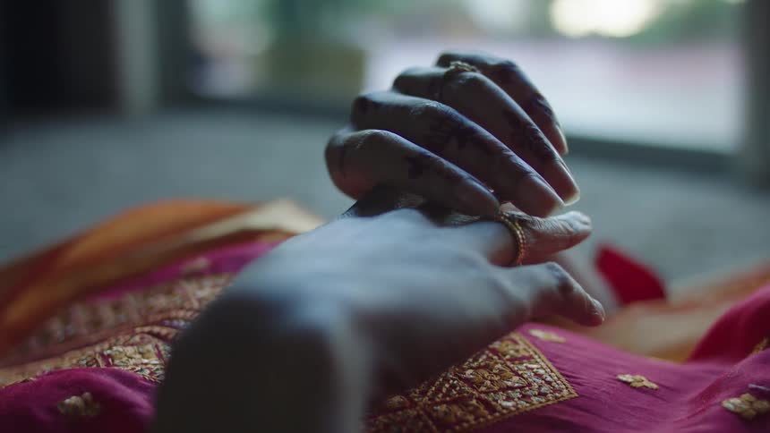 Woman dressed in a gold embroidered outfit with henna designs on her hand lies on her back