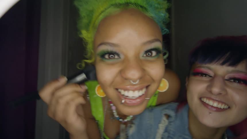 Two happy friends playfuly applying makeup in front of the camera
