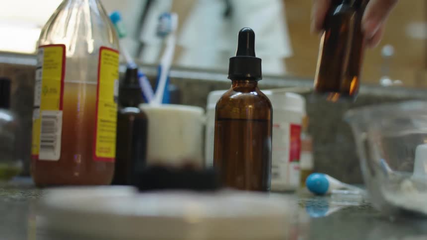 Hand picks up a brown glass bottle from the bathroom counter top