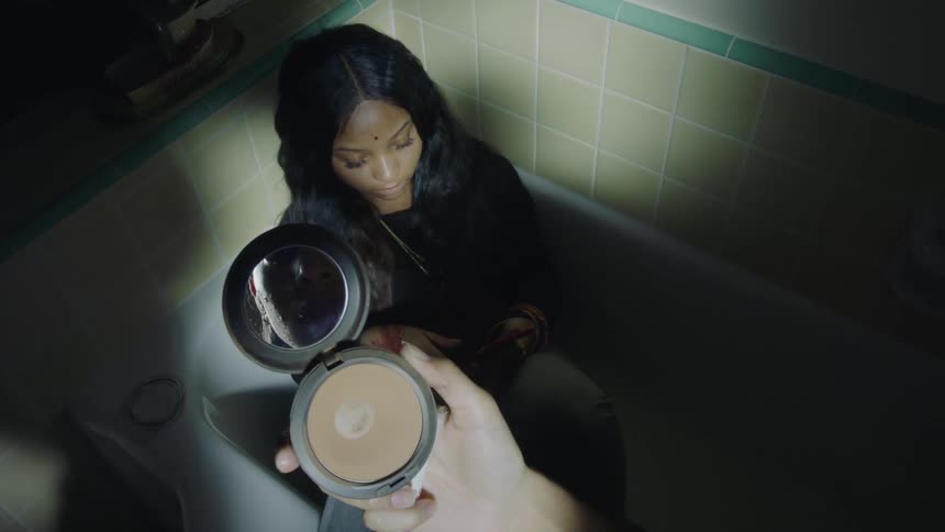 Young girl sitting on an empty bathtub applying makeup in front of a friend