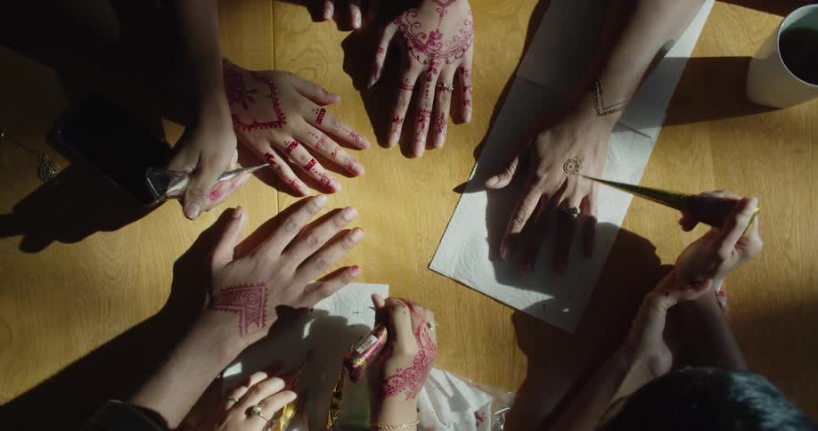 Group of people applying henna ink tattoos on the hands of friends or customers over a table