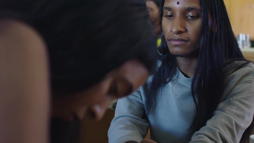 A woman applying a henna tattoo to the hand of an androgynous hindu person with bindi on their forehead