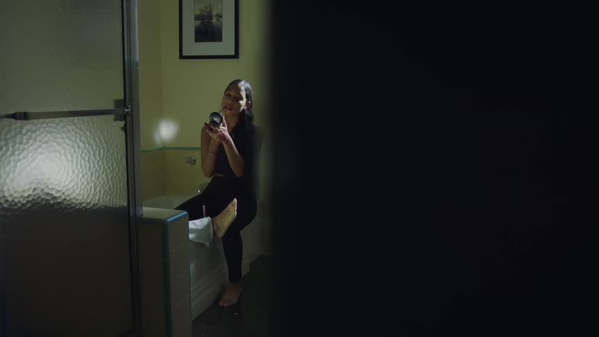 A woman is sitting in the bathroom and putting on makeup