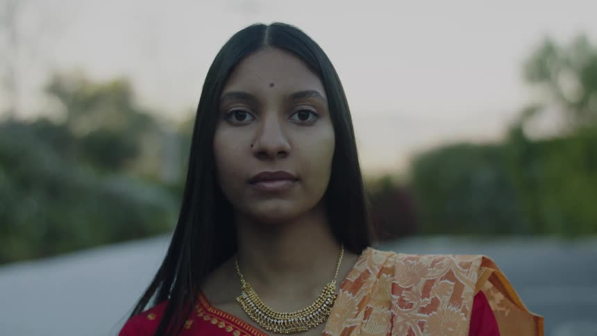 Woman wearing gold necklace and orange sari poses outdoors