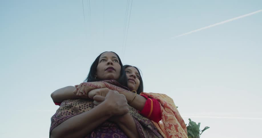 Friends stand outdoors hugging with electric transmission tower in background