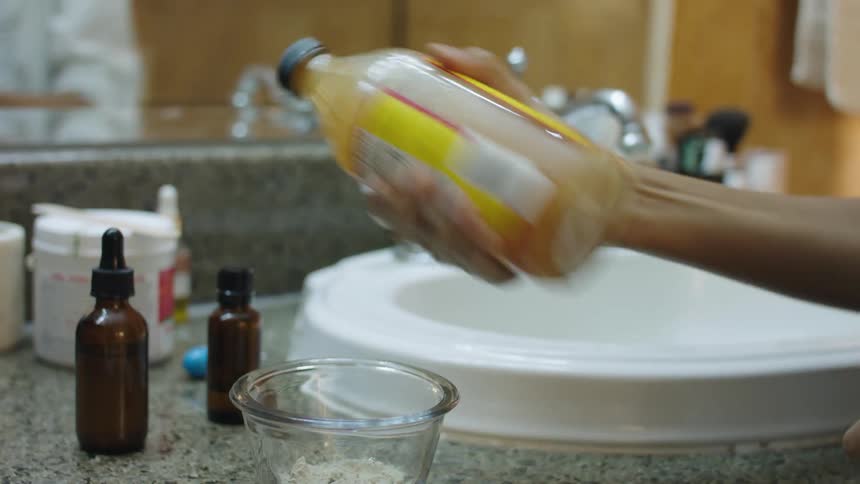 A person shakes a bottle by the sink