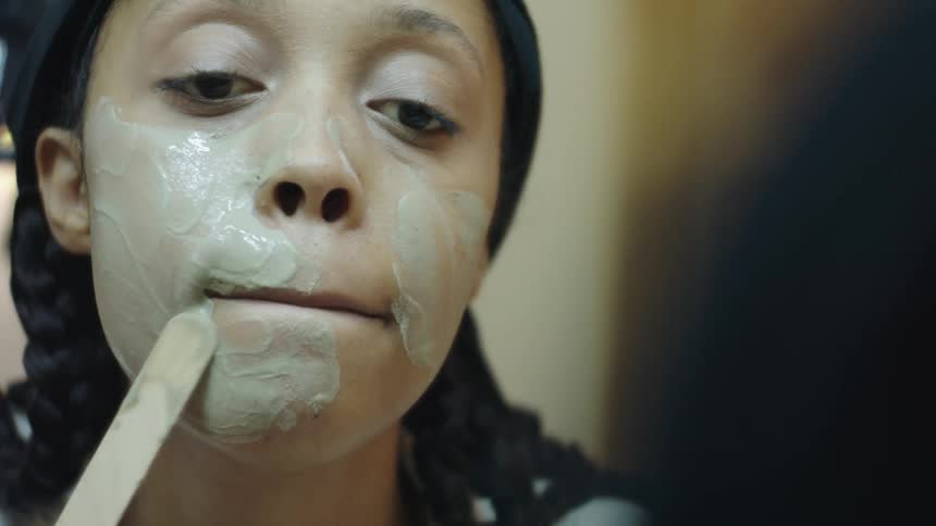 A woman is putting on face cream and looking in the mirror