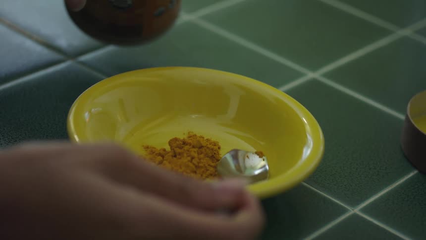 Someone puts a spoonful of cereal into a yellow bowl