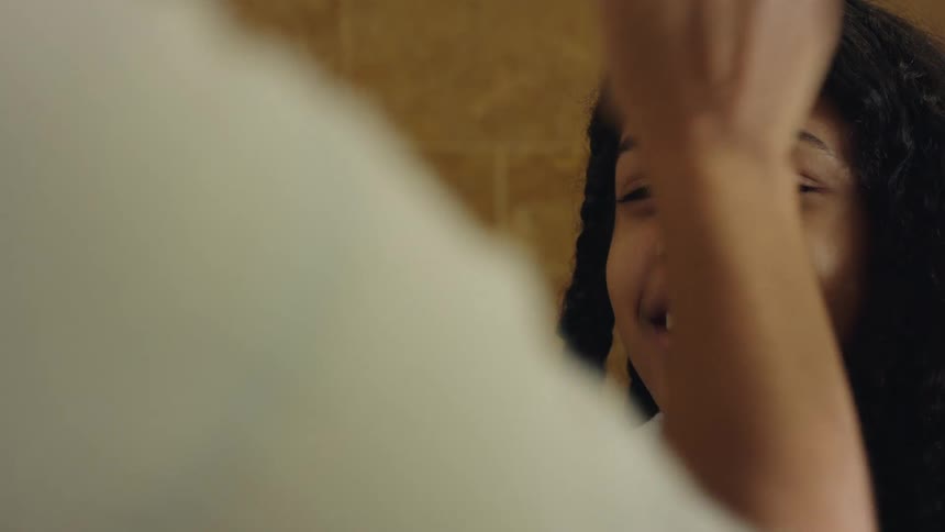 Three girls stand in a bathroom and one girl sprays her little sister in the face with a mist and then waves her hand to dry it as they all laugh