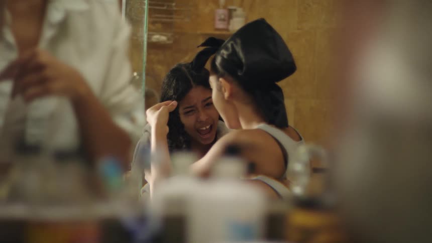 Three girls are doing their hair in a mirror