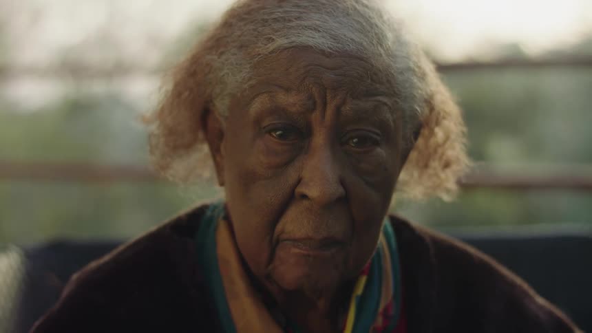 Elderly woman sits outdoors looking straight ahead