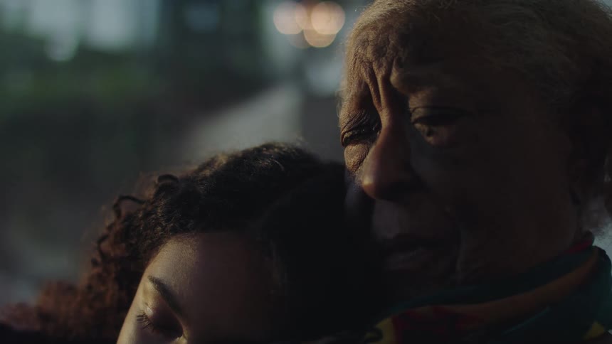 An elderly woman is holding a teenage girl as they relax