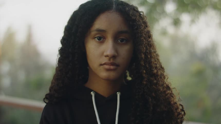A teenage girl in a hoodie smiling outside for a portrait