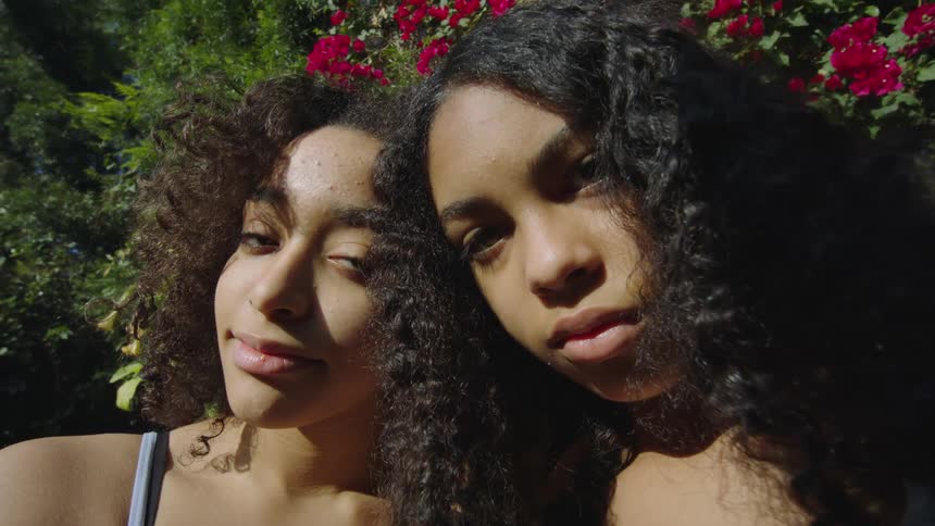 Two women posing with their heads leaning together in the bright sunshine