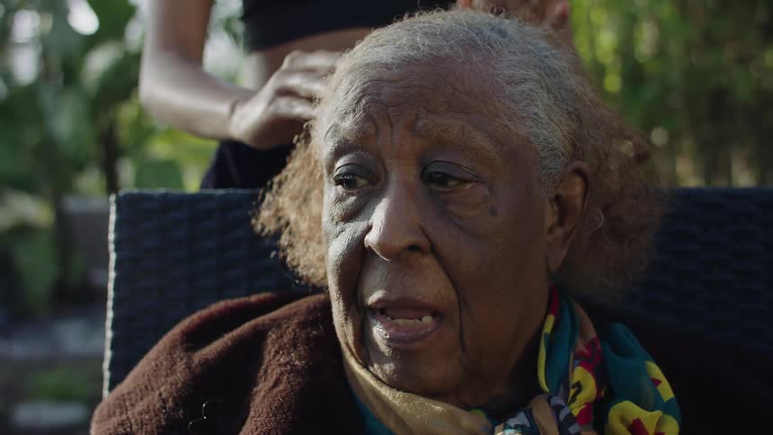 Young woman rubs the hair of an elderly mother sitting on a chair outdoors