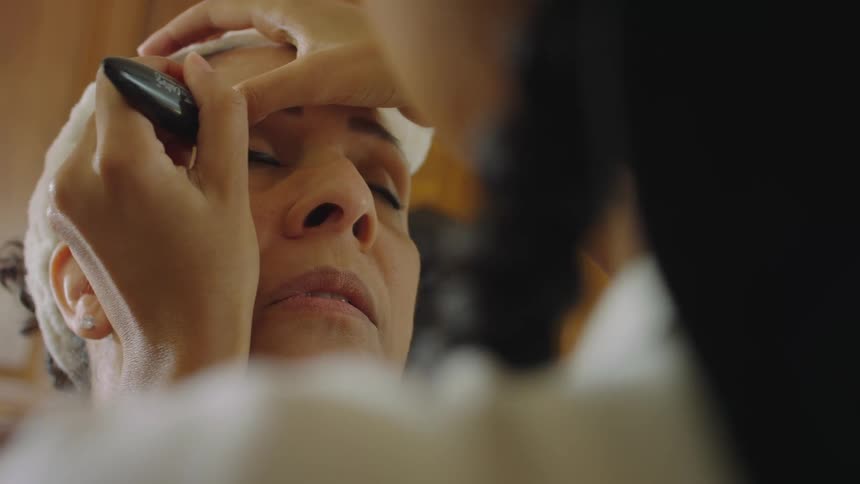Two women are indoors and applying makeup