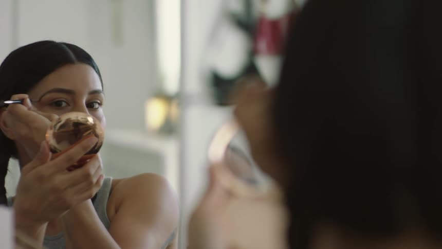 A woman with dark braids applying makeup indoors