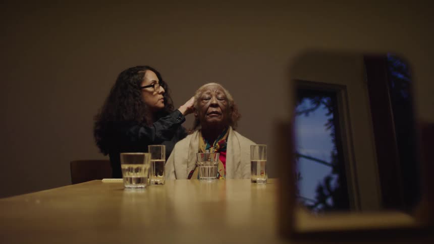 Woman with curly hair and glasses does elderly womans gray hair sitting at table with glasses