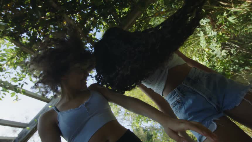 Two teenage girls stands outside and fling their hair in the air
